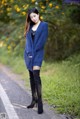 A woman in a blue sweater and black boots standing on a road.