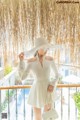 A woman in a white dress and hat standing on a balcony.