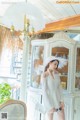 A woman in a white dress and hat standing in front of a cabinet.