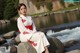 A woman in a white and red kimono sitting on a rock by a river.