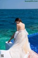 A woman in a white dress sitting on the edge of a swimming pool.