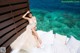 A woman in a wedding dress sitting on a bed by the ocean.