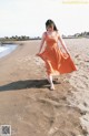 A woman in an orange dress walking on the beach.