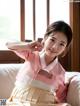 A young girl in a pink and beige hanbok sitting on a bed.