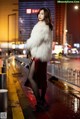 A woman in a white fur coat standing on a city street.