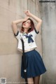 A woman in a school uniform leaning against a wall.