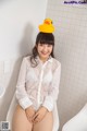 A woman sitting on a toilet with a rubber duck on her head.