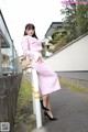 A woman in a pink dress leaning against a fence.