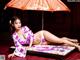 A woman in a kimono laying on a bed under an umbrella.