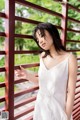 A woman in a white dress leaning against a red fence.