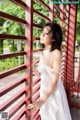 A woman in a white dress leaning against a red fence.