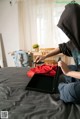 A person in a hoodie sitting on a bed with a suitcase.