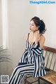 A woman sitting on a wooden bench wearing a striped dress.