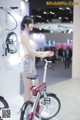 A woman standing next to a bike on display.