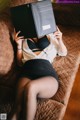 A woman laying on a couch holding a book over her head.