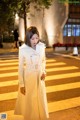 A woman in a white trench coat standing on a crosswalk.