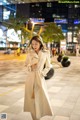 A woman in a white trench coat is walking down the street.