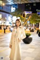 A woman in a white trench coat standing in the middle of a street.