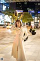 A woman in a white trench coat standing on a city street.