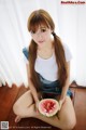 A woman sitting on the floor holding a slice of watermelon.