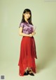 A woman in a purple shirt and red skirt holding a book.