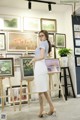 A woman standing in front of a wall of paintings.