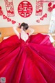 A woman in a red dress sitting on a bed.