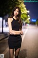 A woman in a black dress standing on a street at night.