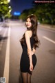 A woman in a black dress standing on the side of a road.