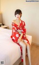 A woman in a red kimono sitting on a bed.