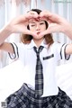 A woman in a school uniform making a heart with her hands.