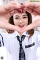 A woman in a school uniform making a heart with her hands.