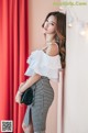 A woman leaning against a wall wearing a white top and black and white skirt.