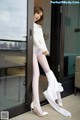 A woman in white stockings and high heels leaning against a glass door.