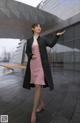 A woman in a pink dress and black coat standing in the rain.