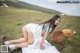 A woman in a white dress sitting on a blanket in a field.