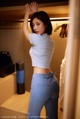 A woman in a white top and blue jeans standing in front of a closet.