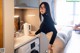 A woman in a black top and beige skirt standing next to a washing machine.