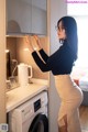 A woman in a black top and beige skirt standing next to a washing machine.