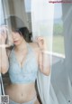 A woman in a blue bra and panties leaning against a window.