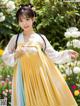 A woman in a yellow and blue hanbok standing in a garden.