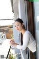 A woman leaning against a window with her hands clasped together.